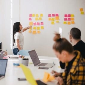 Foto: Frau steht vor Wand mit Post-It´s und moderiert einen Workshop