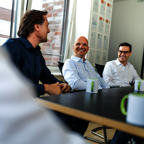 Foto: Zwei Bereichsleiter sind in einem lockeren Gespräch mit dem Geschäftsführer von atlantis dx, sitzen an einem Tisch, lachen sich an