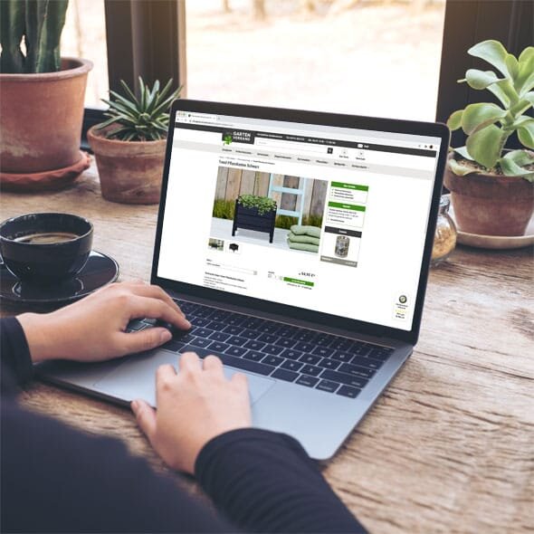 Laptop mit geöffnetem Online-Shop auf einem Schreibtsich aus Holz mit Grünpflanzen auf dem Tisch