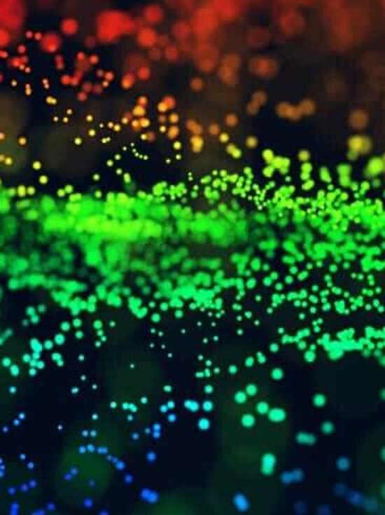 Abstrakt: Blaue, grüne und rote Punkte fließen in eine Richtung auf dunklem Hintergrund