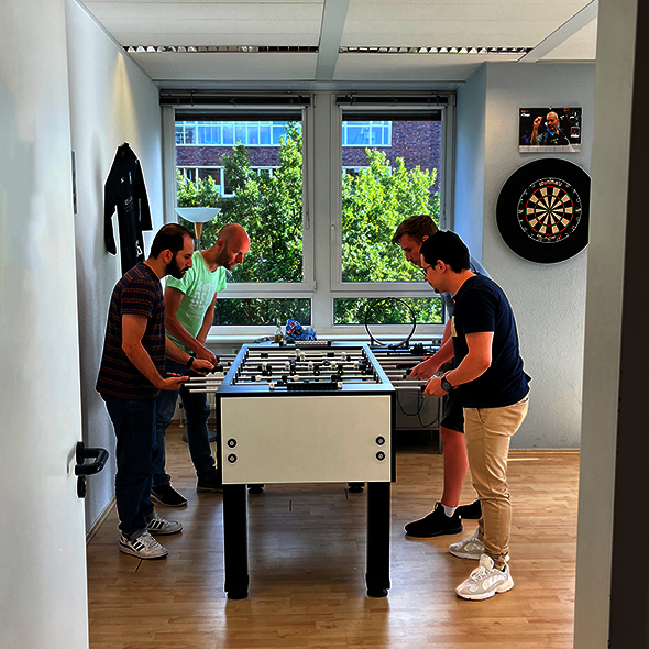 Foto: Vier Mitarbeiter spielen Fußballkicker im Pausenraum
