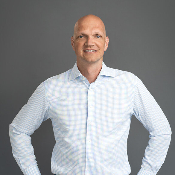 atlantis dx - Denis Rathig, Geschäftsleitung | Partner Foto: Frontalaufnahme von Denis Rathig, lächelt, weißes Hemd, Hintergrund dunkel