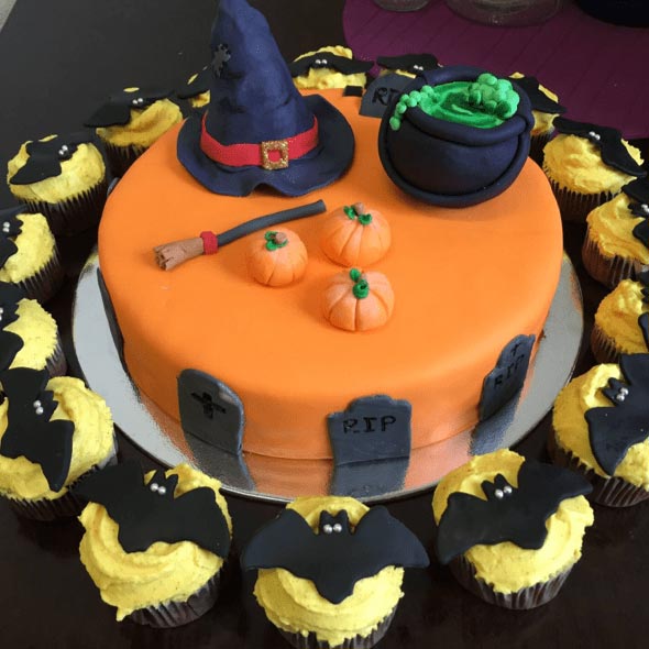 Nahaufnahme Halloweenkuchen in orange mit Hexenhut und Kessel, um den Kuchen verteilt sind  Cupcakes mit Fledermäusen