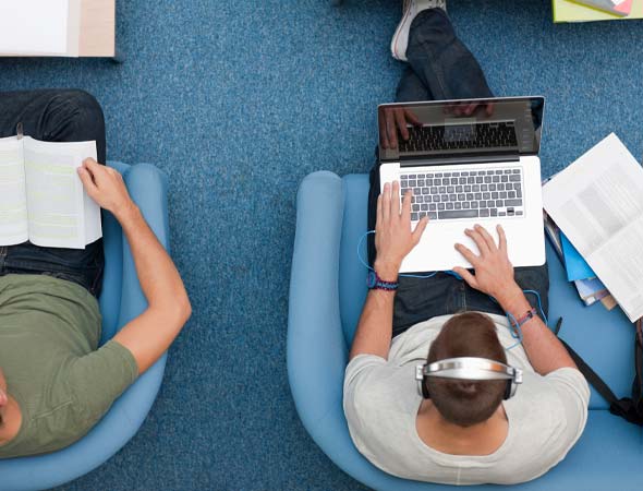 Foto: Sicht von oben auf zwei Studierende, die Laptops auf dem Schoß haben